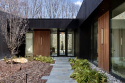 entry to a modern home with a figure walking past the glass front door captured by Andy Frame Photography