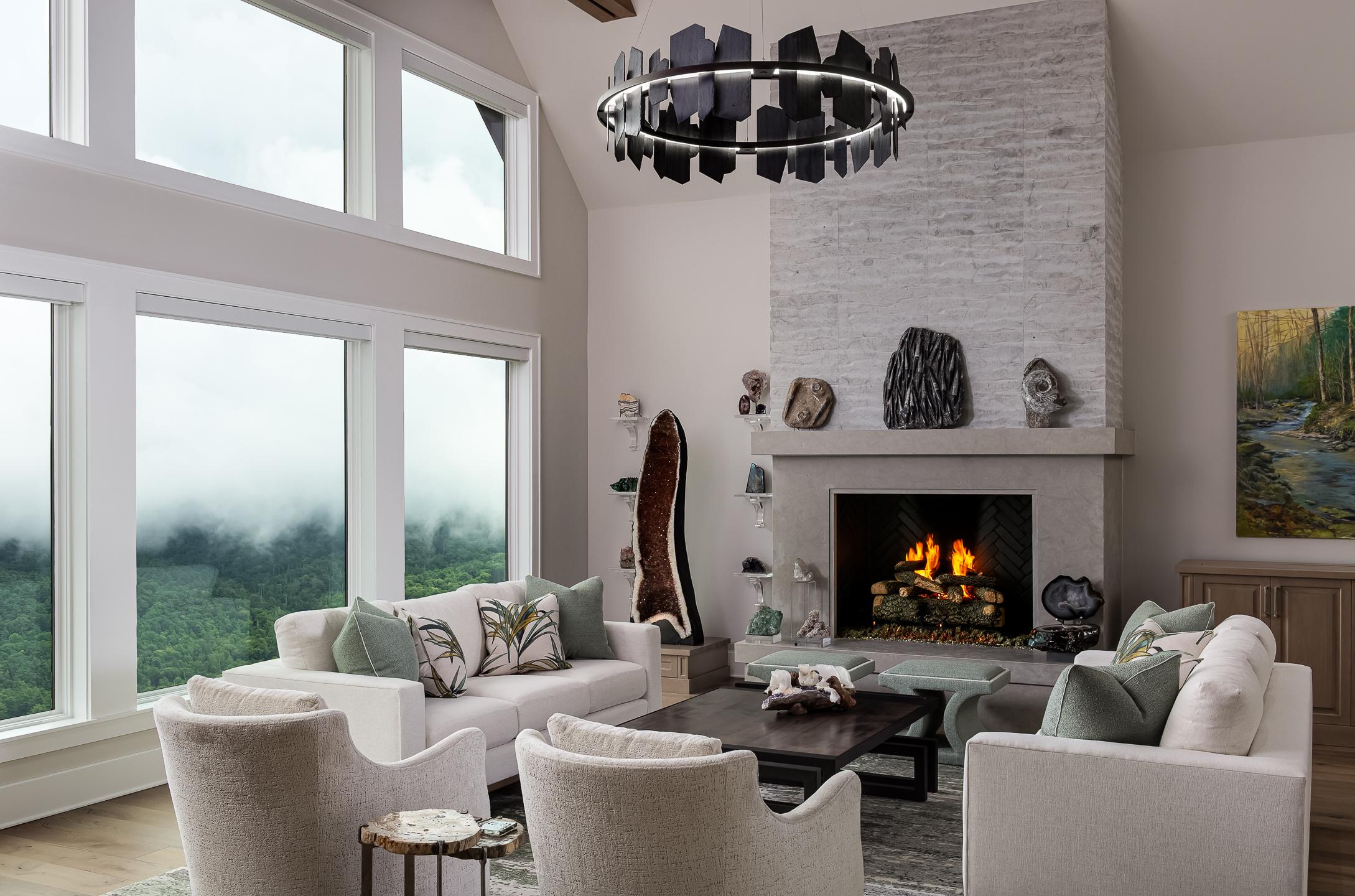 A modern living room with large windows, a fireplace, and comfortable seating. The room features a high ceiling, contemporary chandelier, and a view of North Carolina's lush landscape with mist-covered hills—perfect for architectural photography aficionados. captured by professional architectural photographer