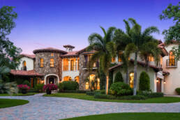a large mansion with a driveway and palm trees.