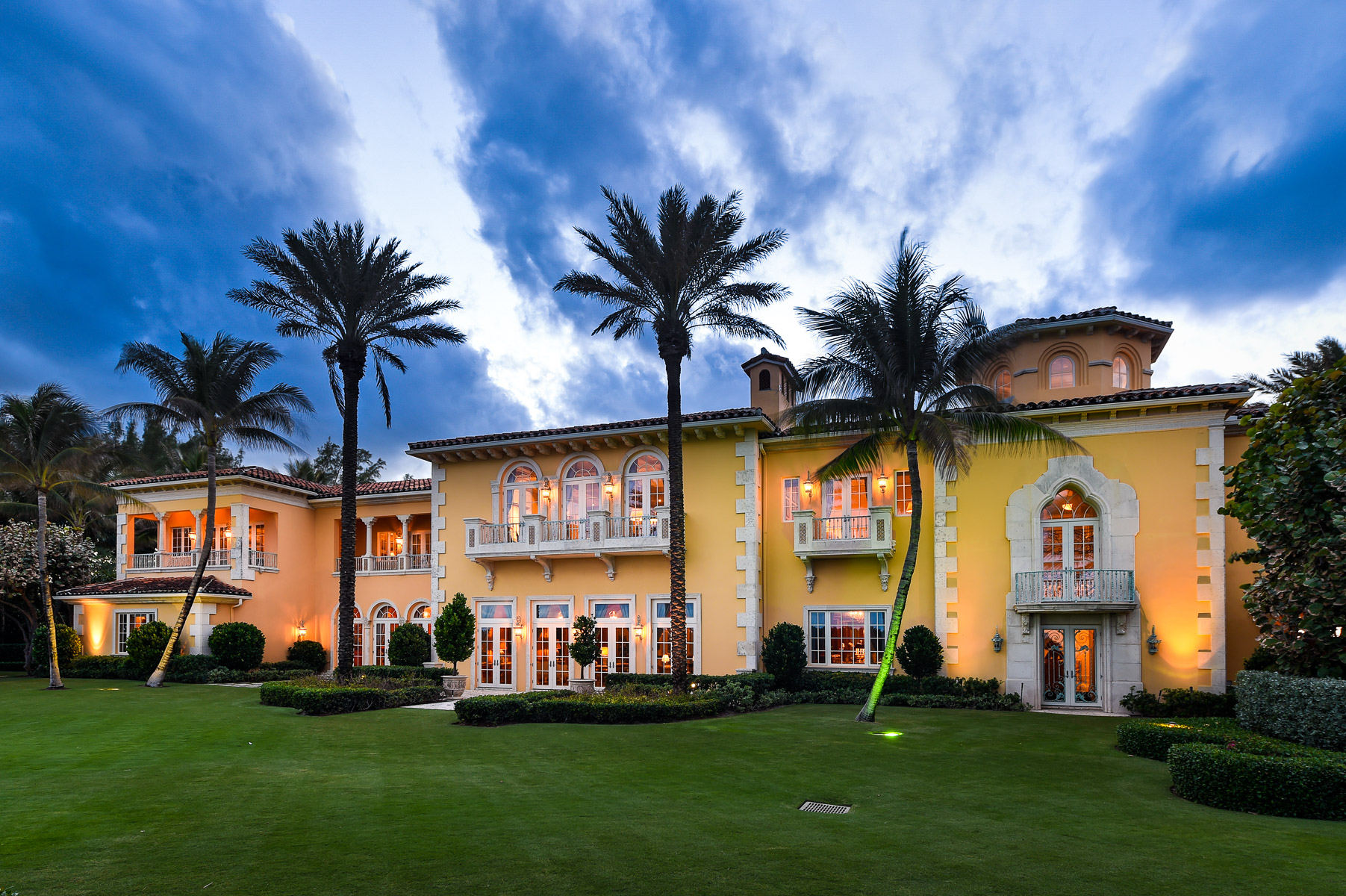 a large yellow mansion with palm trees on the lawn.