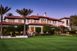 a large mansion with a lawn and palm trees.