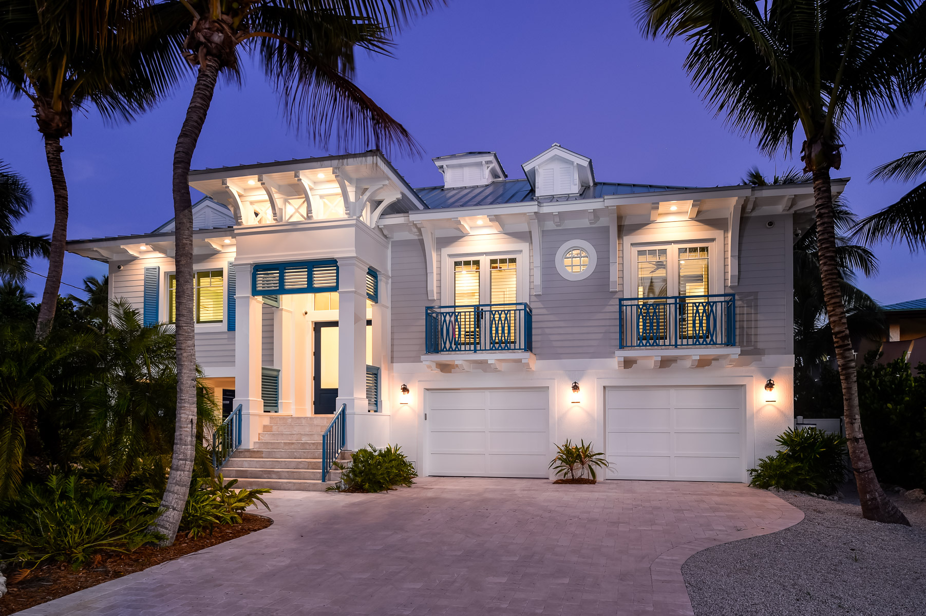 a white and blue home with palm trees at dusk.