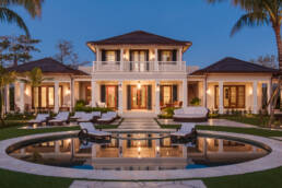 a white house with a pool and lounge chairs at dusk.